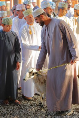 NIZWA, AL DAKHILIYAH, OMAN - 20 ARALIK 2024: Kalabalık keçi pazarı, Omani erkek ve çocukların geleneksel kıyafetleri ve keçi müzayedesinin otantik sahneleri