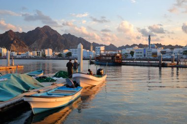 MÜTTRAH, MÜZCAT, OMAN - 26 ARALIK 2024: Balıkçı ağları üzerinde çalışan balıkçılar ve arka planda Muttrah Corniche ile balık pazarına yakın iskele