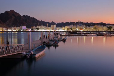 Muttrah Corniche mavi saatte balık pazarının yanındaki iskeleden görüldü. Arka planda cami ve dağlar vardı. Muttrah, Muscat, Umman.