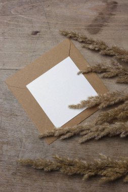 Kahverengi bir zarfın üzerinde boş bir kart ve yanında da kuru otlar var. 