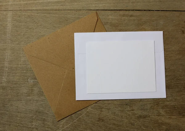 木のテーブルの上に白と茶色の封筒の上に白いカード — ストック写真