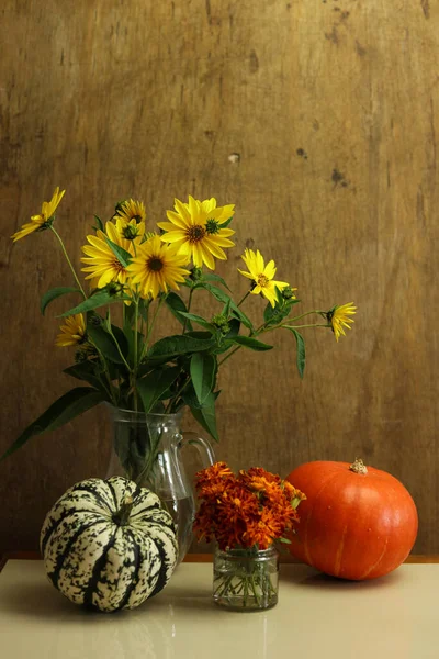a still life with wild sunflowers in a vase and colorful pumpkins