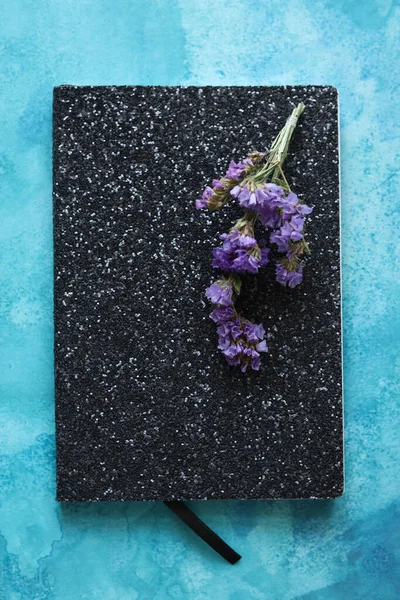 black glitter notepad with purple dried flowers on top with a watercolor background
