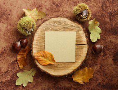 Kestaneli ve sonbahar yapraklı, kahverengi suluboya arka planda bir tahta parçasında boş bir not kartıyla durgun bir hayat.