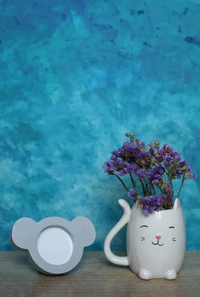 an empty picture frame and a cat Vase with statice flowers on wooden table against blue wall background, mock up