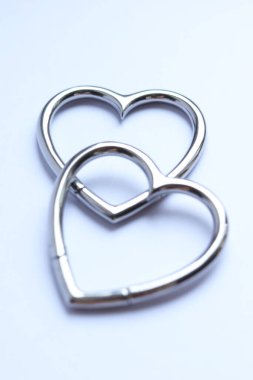 Beyaz arka planda kalp şeklinde paslanmaz çelik küpeler.