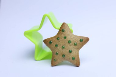 Green star shaped cookie cutter and gingerbread cookie on white background. christmas concept clipart