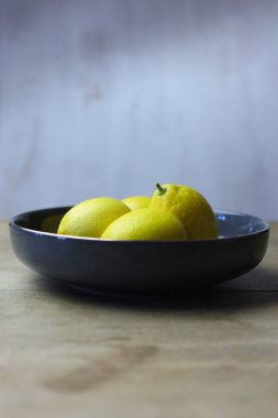 Tahta bir masada ve beyaz arka planda bir kasede limonlar