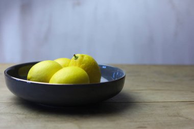Tahta bir masada ve beyaz arka planda bir kasede limonlar