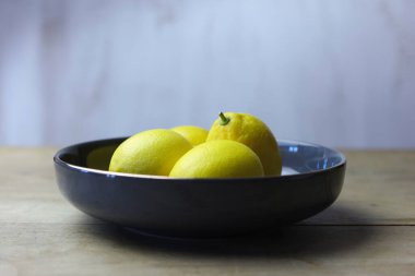 Tahta bir masada ve beyaz arka planda bir kasede limonlar