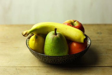 Tahta masadaki bir kasede taze meyvelerle dolu bir hayat seçici bir odak noktası.