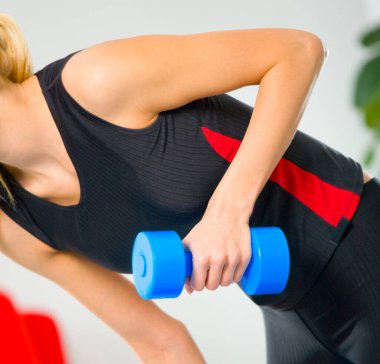 Spor kıyafetli bir kadın, spor salonunda halterlerle spor yapıyor.