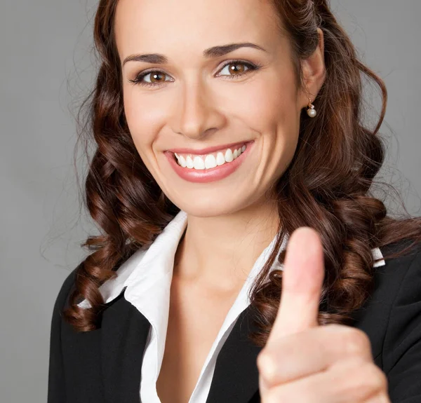 幸せな笑みを浮かべて陽気な若い女性実業家グレーバック グラウンド以上のジェスチャでは 親指を示す — ストック写真