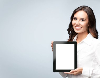 Gülümseyen genç esmer iş kadını boş isimsiz tablet pc monitörü gösteriyor, gri arkaplan üzerinde, slogan ya da kısa mesaj için telif alanı var. Stüdyo çekimlerinde başarı. 