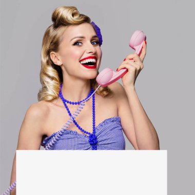 Telefon ve boş tabela ile güzel genç mutlu gülümseyen kadın Portresi, pin-up tarzı giyinmiş. Retro moda ve vintage konsept stüdyo çekimi poz Kafkas sarışın modeli, gri arka plan üzerinde.