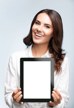 Gülümseyen esmer iş kadını, gri arkaplan üzerinde isimsiz tablet pc monitörü ve slogan ya da kısa mesaj için telif alanı gösteren mutlu bir iş kadını. Stüdyo çekimlerinde başarı. 