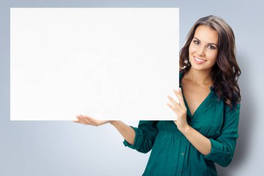 Mutlu, kendine güvenen, yeşil elbiseli genç bir kadın, gri arkaplan üzerinde bir metin ya da slogan için boş alanlı boş tabela gösteriyor. İş ve reklam konseptinde başarı.