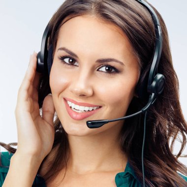 Mutlu gülümseyen güzel telefon operatörünün portresi kulaklık takmış, yeşil kendine güvenen kıyafetler, gri arka planda. Çağrı merkezi ve müşteri destek servisi kavramı.