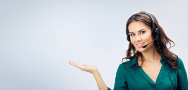 Mutlu gülümseyen güzel kadın telefon operatörünün portresi. Yeşil, kendine güvenen giysiler içinde. Gri arka planda. Çağrı merkezi ve müşteri destek servisi kavramı.