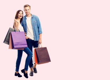 Alışveriş çantalı mutlu bir çift, birbirine yakın duruyorlar, slogan ya da reklam mesajı için boş bir alana sahipler, pembe arka planda. Aşıkta beyaz modeller, tatil satışları, dükkan, perakende, tüketici konsepti.