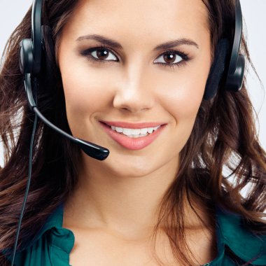 Mutlu gülümseyen güzel telefon operatörünün portresi kulaklık takmış, yeşil kendine güvenen kıyafetler, gri arka planda. Çağrı merkezi ve müşteri destek servisi kavramı.