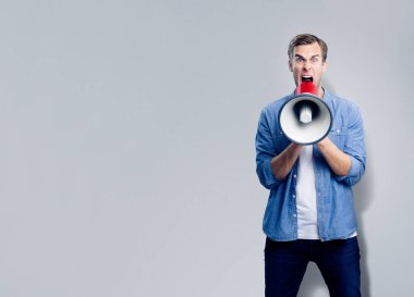 Man shouting through megaphone, with empty copyspace area for slogan, advertising or text message, over grey background. Caucasian male model in blue smart casual clothing making announcement, studio concept. clipart