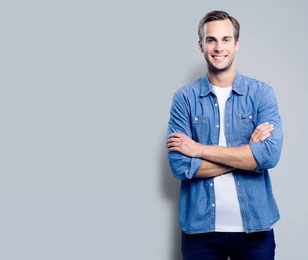 stock image Portrait of happy smiling man standing in crossed arms pose, with empty copyspace area for slogan, advertising or text message, over grey background. Caucasian male model in smart casual clothing, studio shoot.