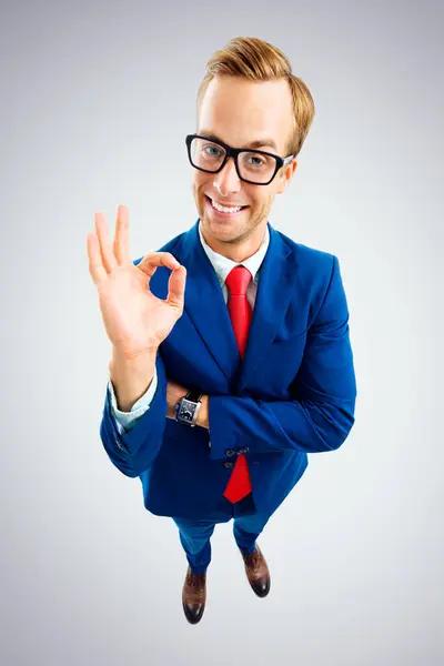 穿着眼镜 蓝色西服 打着红色领带的滑稽的快乐商人的画像 在灰色背景下表现出可以接受的姿势或零 顶角镜头 业务概念 图库图片