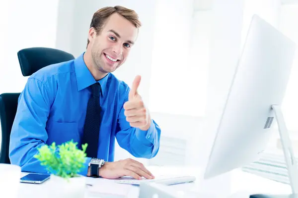 穿着自信衣服 蓝色衬衫 打领带 面带微笑的快乐商人形象 带着大拇指 与办公室的台式电脑一起工作 工作和教育概念方面的成功 — 图库照片