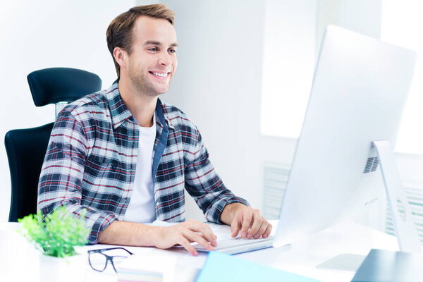 Happy smiling young man in casual smart clothing, working with desktop computer at office. Success in business, job and education concept.