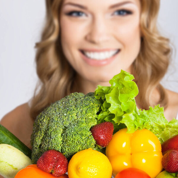 Cheerful young beautiful woman with healthy vegetarian raw food, over gray. Selective focus on food.