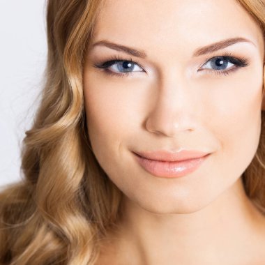 Gri arka planda gülümseyen bir kadının portresi.