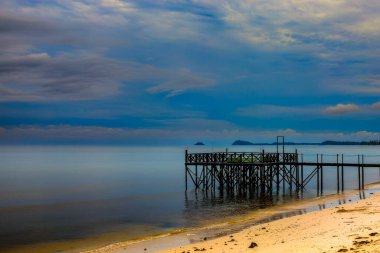 Arka planda gökyüzü olan kumlu bir sahilde ahşap bir iskele.