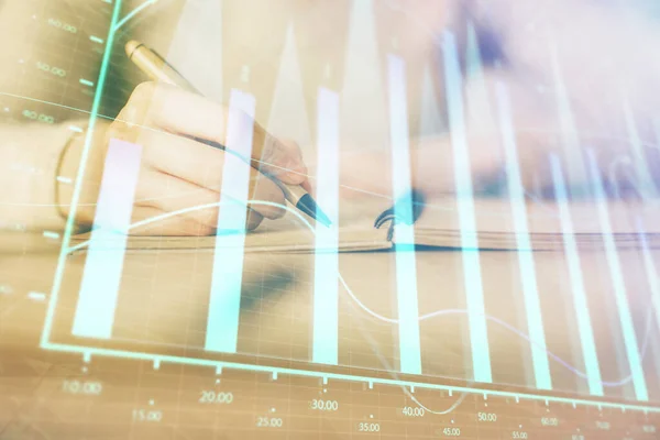 Stock image Hands writing information about stock market in notepad. Forex chart holograms in front. Concept of research. Multi exposure