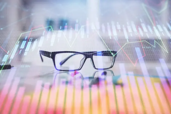 テーブルの上に眼鏡をかけた金融グラフのホログラム ビジネスの概念 二重露光 — ストック写真
