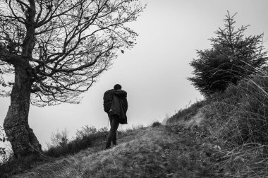 Aktif eğlence. Sırtında sırt çantası olan bir adam dağın tepesinde, dağ boyunca yürür, sis, bulutlu, dağa tırmanır. Tatilde. Seçici odak, doğa