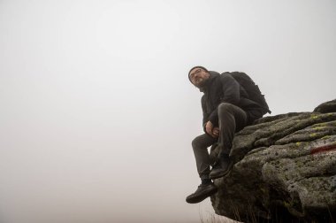 Gözlüklü ve sakallı genç bir adam, bir gezgin, bir dağın kenarında oturur, sis, sis, dağlarda dinlenir. Yazmak için boş alan