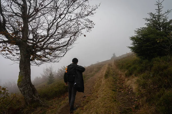 A man with a backpack on his back walks along the path, the top of the mountain, fog, cloudy. Recreation. Selective focus, nature