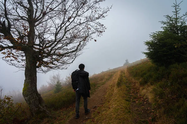 Active recreation. A man with a backpack on his back walks along the path, the top of the mountain, fog, cloudy, climbing the mountain. Vacation. Selective focus, nature