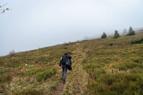 A man with a backpack on his back walks along the path, the top of the mountain, fog, cloudy. Recreation. Selective focus, nature