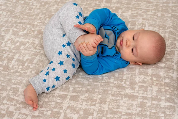 stock image Funny little baby boy wearing a nappy playing with his legs in nursery. Cute kid sucking his feet. Child after bath or shower on bed. Infant skin care