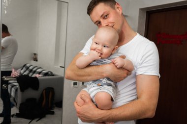 Mutlu bir baba, küçük oğlunu kollarının arasına alır ve gülümser. Mutlu aile, beyler.