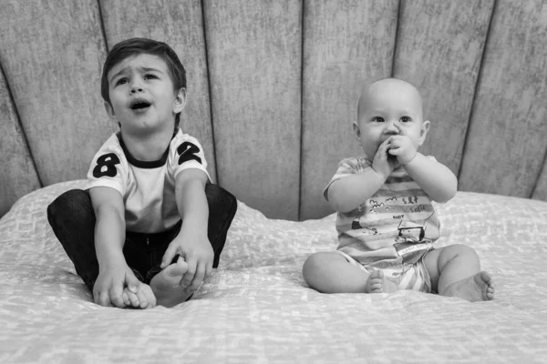 クローズアップ肖像画 2人の兄弟のベッドの上に座って 離れて 笑みを浮かべて 再生します ビューはまっすぐです 二人の男の子がベッドに座っている ベッドの上で一緒に赤ちゃんの男の子と弟 — ストック写真
