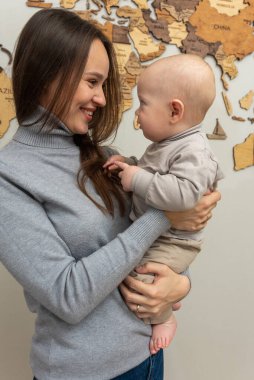 Genç ve güzel anne küçük oğlunu kollarında tutuyor, gülümsüyor, sarılıyor. Genç aile, anne-oğul eğitimi, duygular, sarılmalar.