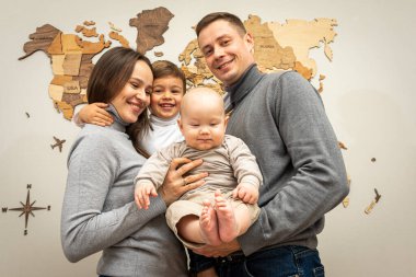 Genç bir ailenin portresi, baba, anne ve iki küçük oğul, neşeli, arkadaş canlısı ve güçlü bir aile. Gülümsüyorlar ve kollarında çocuklara sarılıyorlar. Genç arkadaş canlısı aile kavramı.