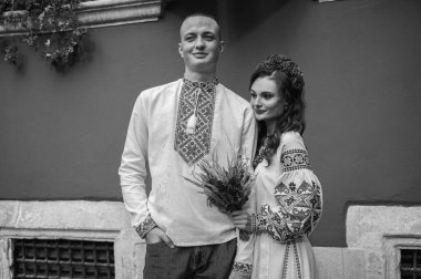 Siyah beyaz portre. Aşık genç bir çift, Ukrayna 'nın işlemeli elbiseleriyle eski şehir Lviv' de yürüyen bir aile, el ele tutuşuyorlar. Gençler eski Lviv kasabasında sarılıyor