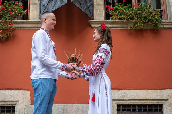 Happy young couple in love, family walking in the old city of Lviv in traditional Ukrainian shirts, holding hands on a red-orange background. Young people hug in the old town of Lviv