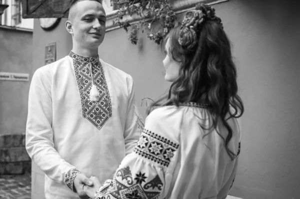 白黒の肖像画 愛の幸せな若いカップル 家族は手を取り合って ウクライナの刺繍のドレスで旧市街のリヴィウを歩く 若い人たちは旧市街で抱擁します — ストック写真