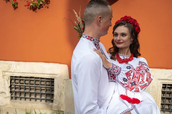 愛の幸せな若いカップル 家族は赤いオレンジの背景に手を取り合って ウクライナの刺繍シャツで旧市街のリヴィウを歩いています 若い人たちは旧市街で抱擁します — ストック写真