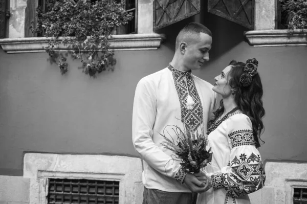 白黒の肖像画 愛の幸せな若いカップル 家族は手を取り合って ウクライナの刺繍のドレスで旧市街のリヴィウを歩く 若い人たちは旧市街で抱擁します — ストック写真